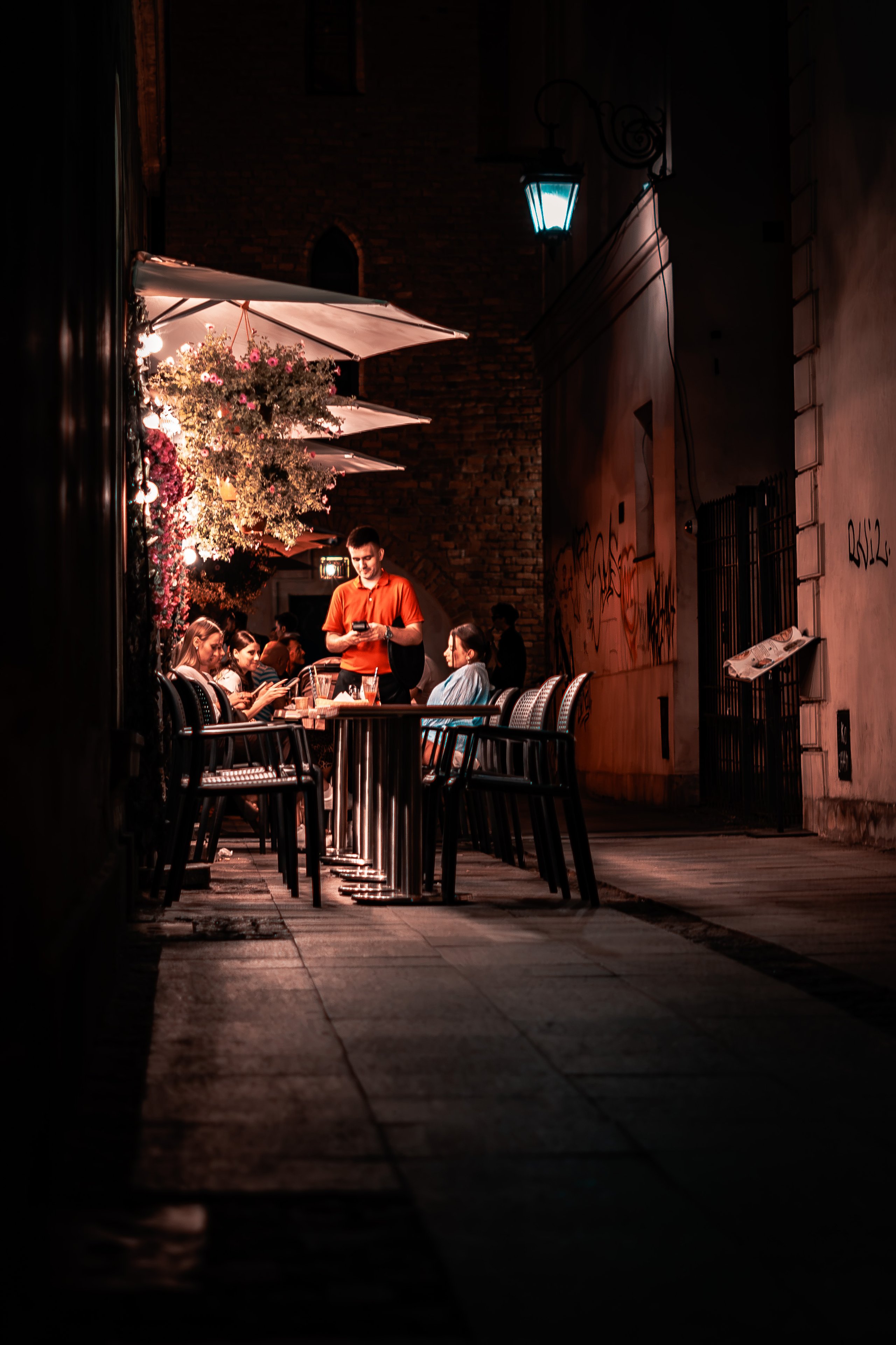 A waiter taking an order at outdoor tables in a narrow lamplit alley