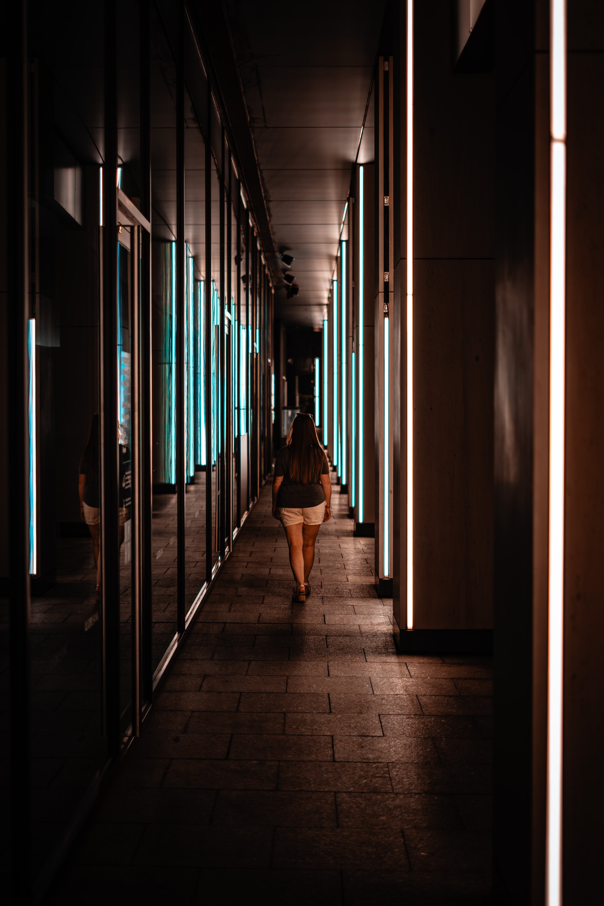 A woman walking a covered walkway lined with vertical light panels at dusk