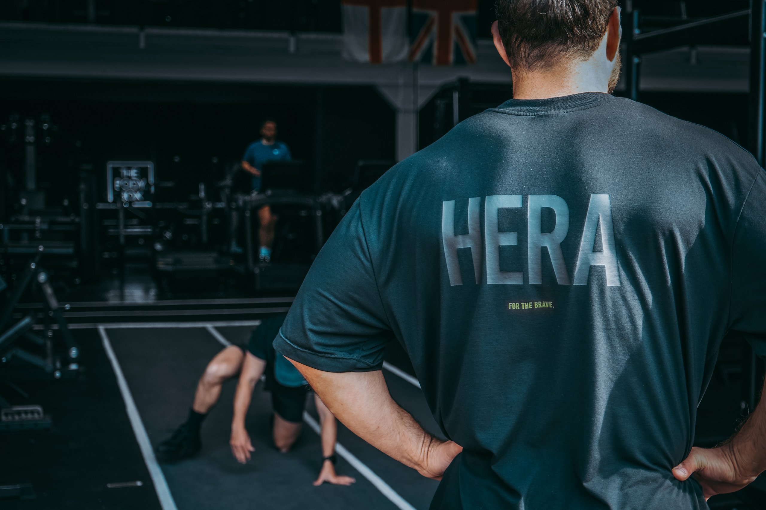 A man in a HERA training top watching an athlete train on the gym floor