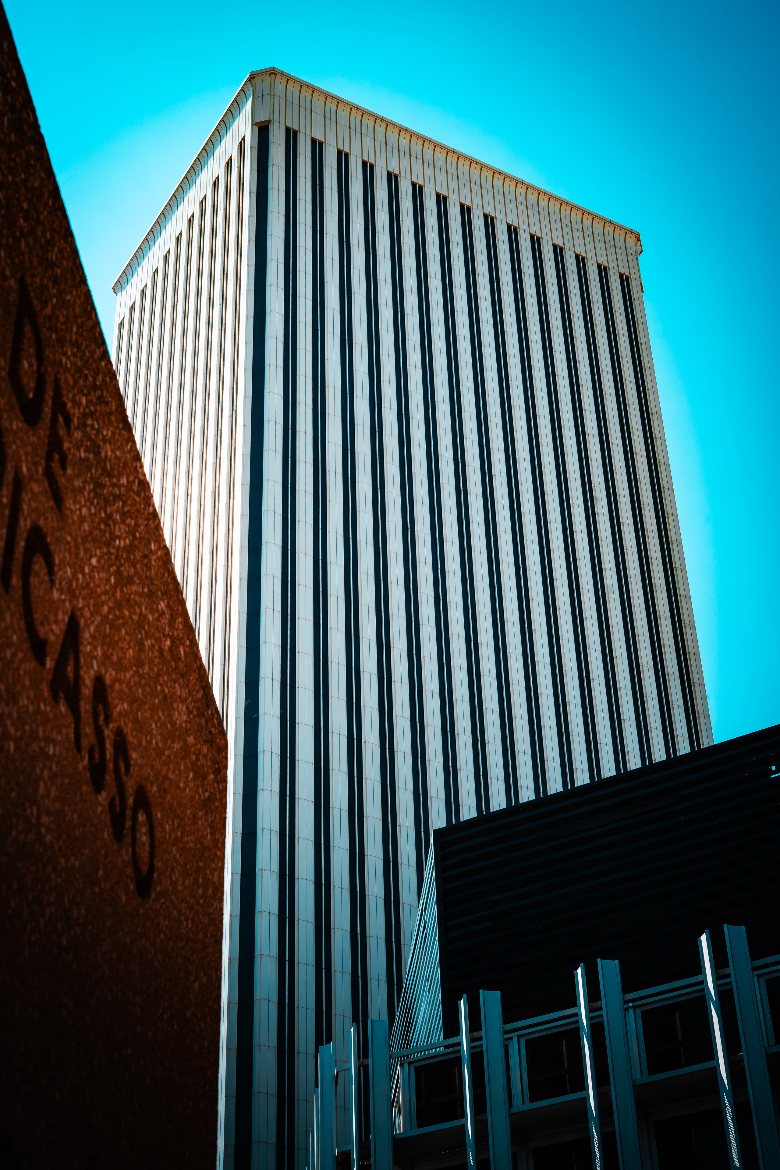 A ribbed white tower against a deep blue sky beside a brick wall