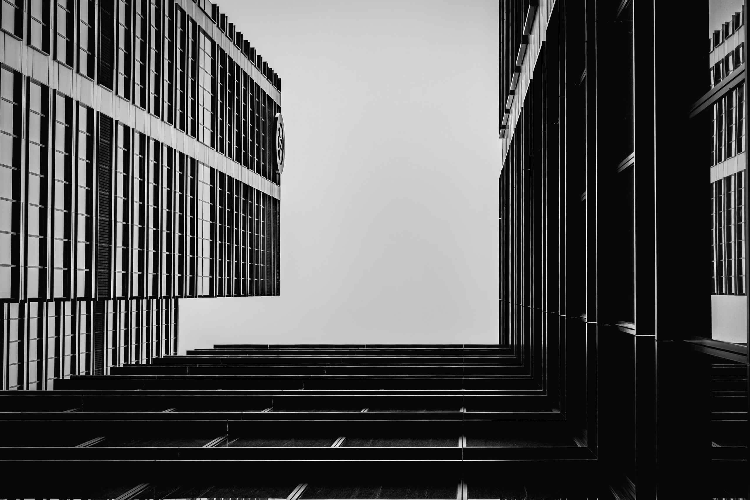 Two office facades framing a bright sky, looking straight up in black and white