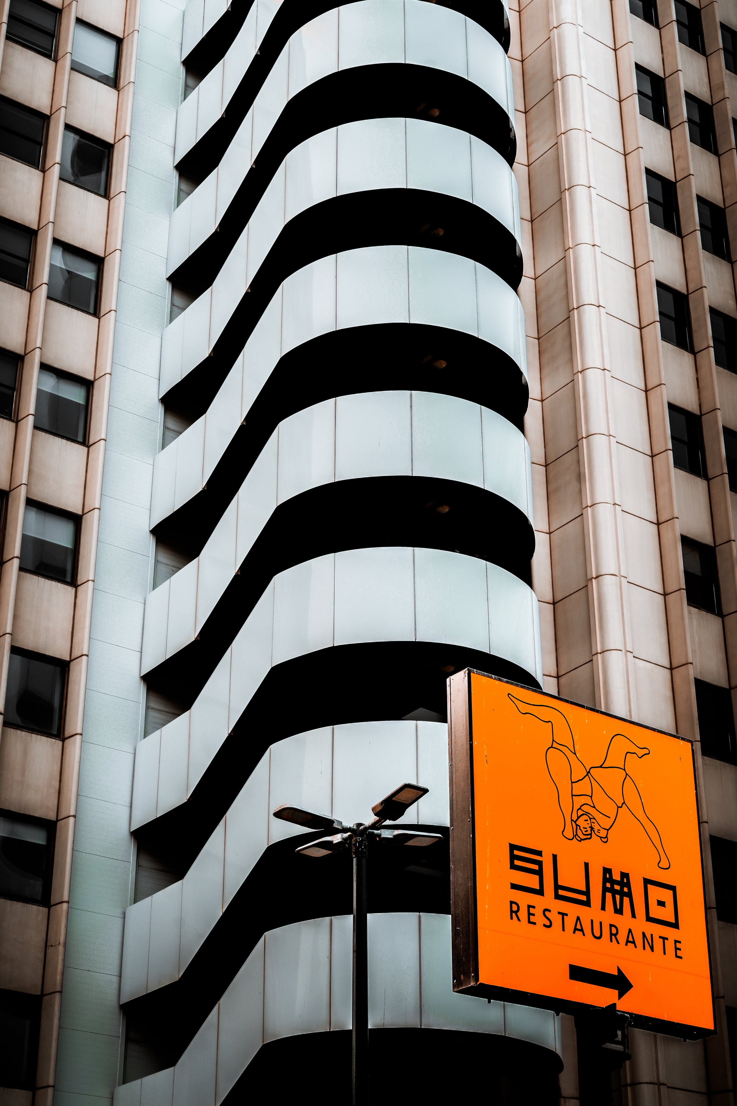 A restaurant sign in front of a tower of curved white balconies