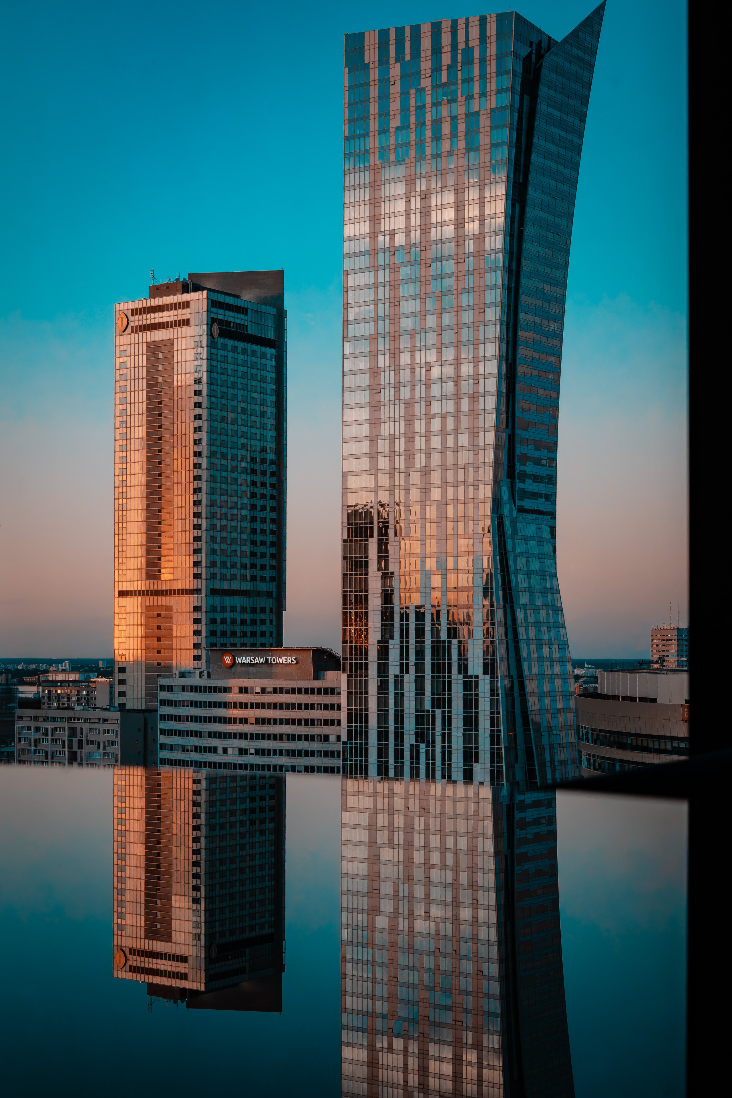 Two high rise towers at sunset, mirrored in still water below