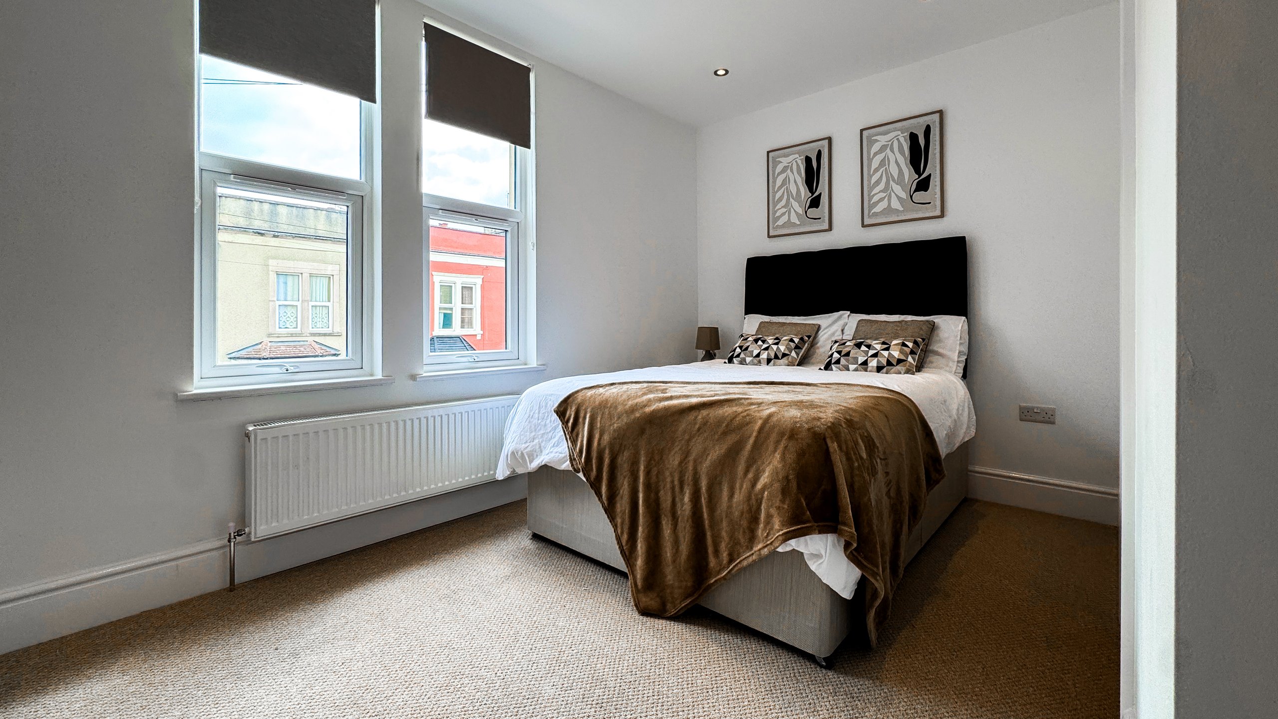 A double bedroom with two windows, a brown throw and framed botanical prints