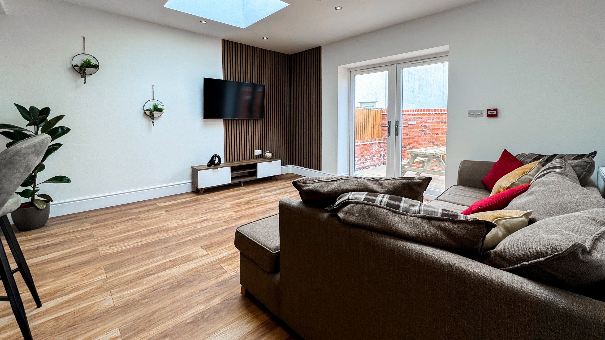 A living area with a corner sofa, wall mounted television and garden doors