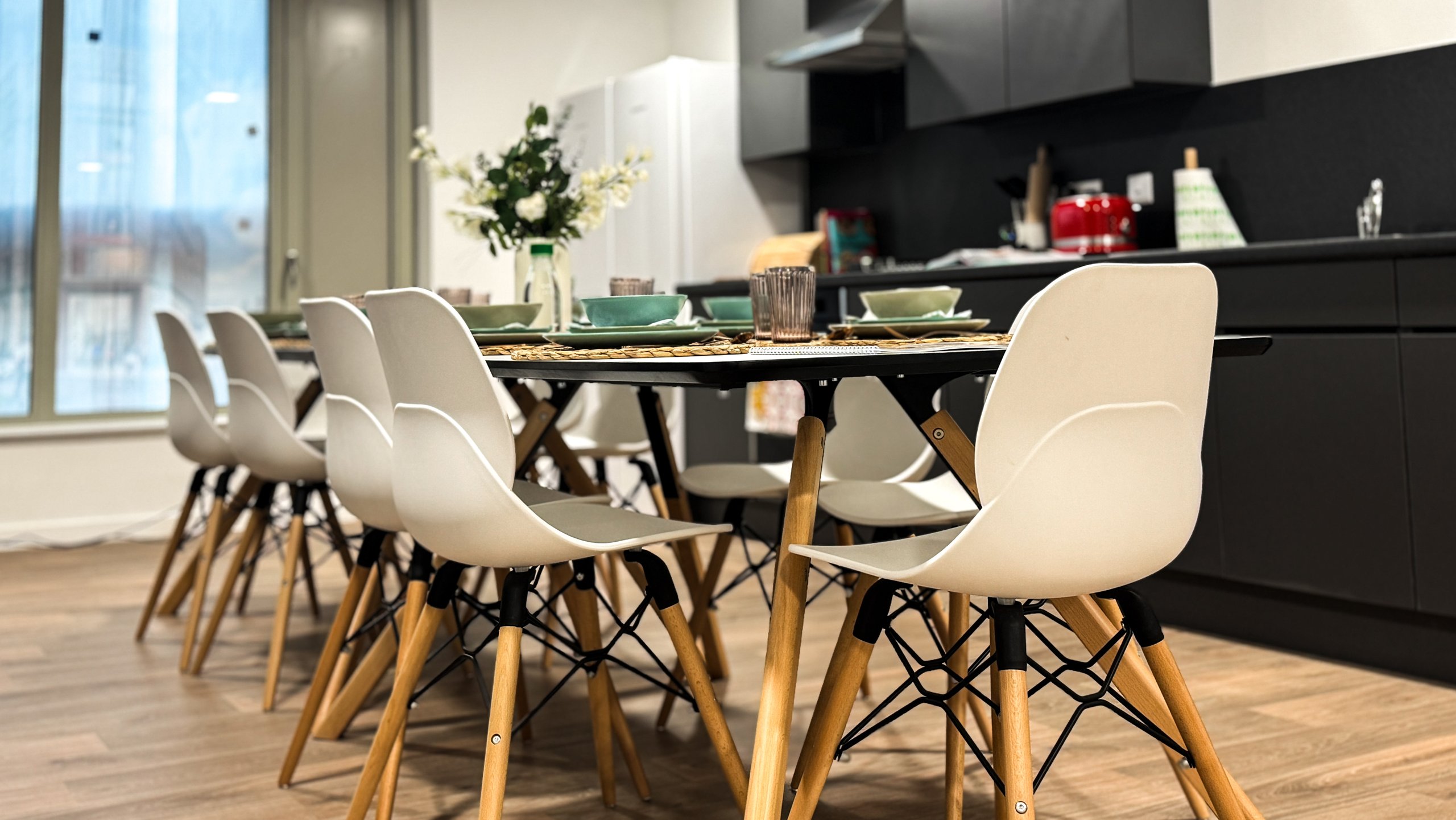 A long communal dining table and white chairs in a shared development kitchen