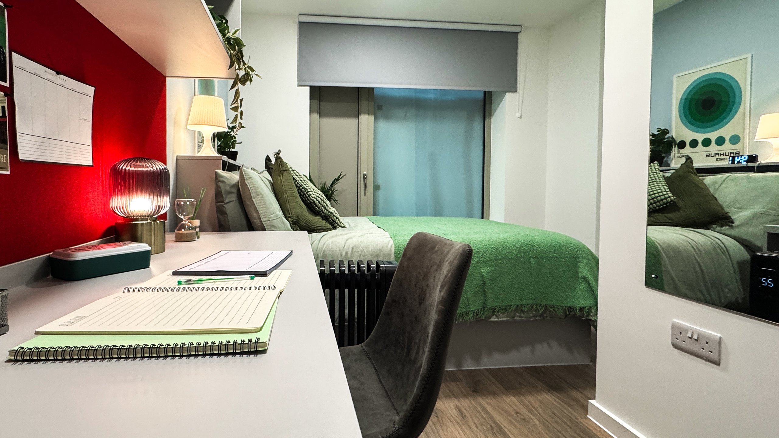 A student room with a study desk, green bedding and a red feature wall