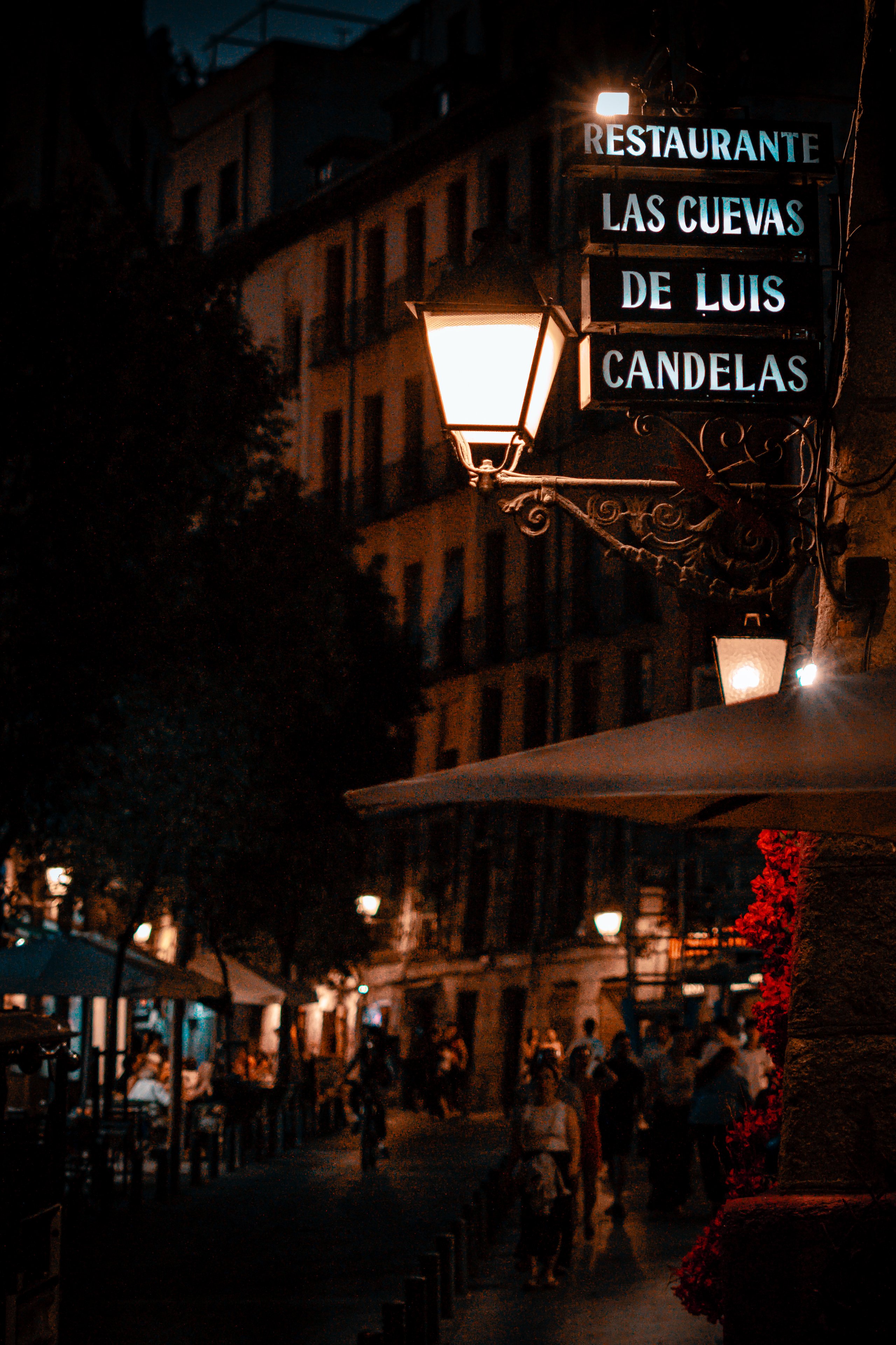 A lit lantern and restaurant sign above busy pavement tables at night