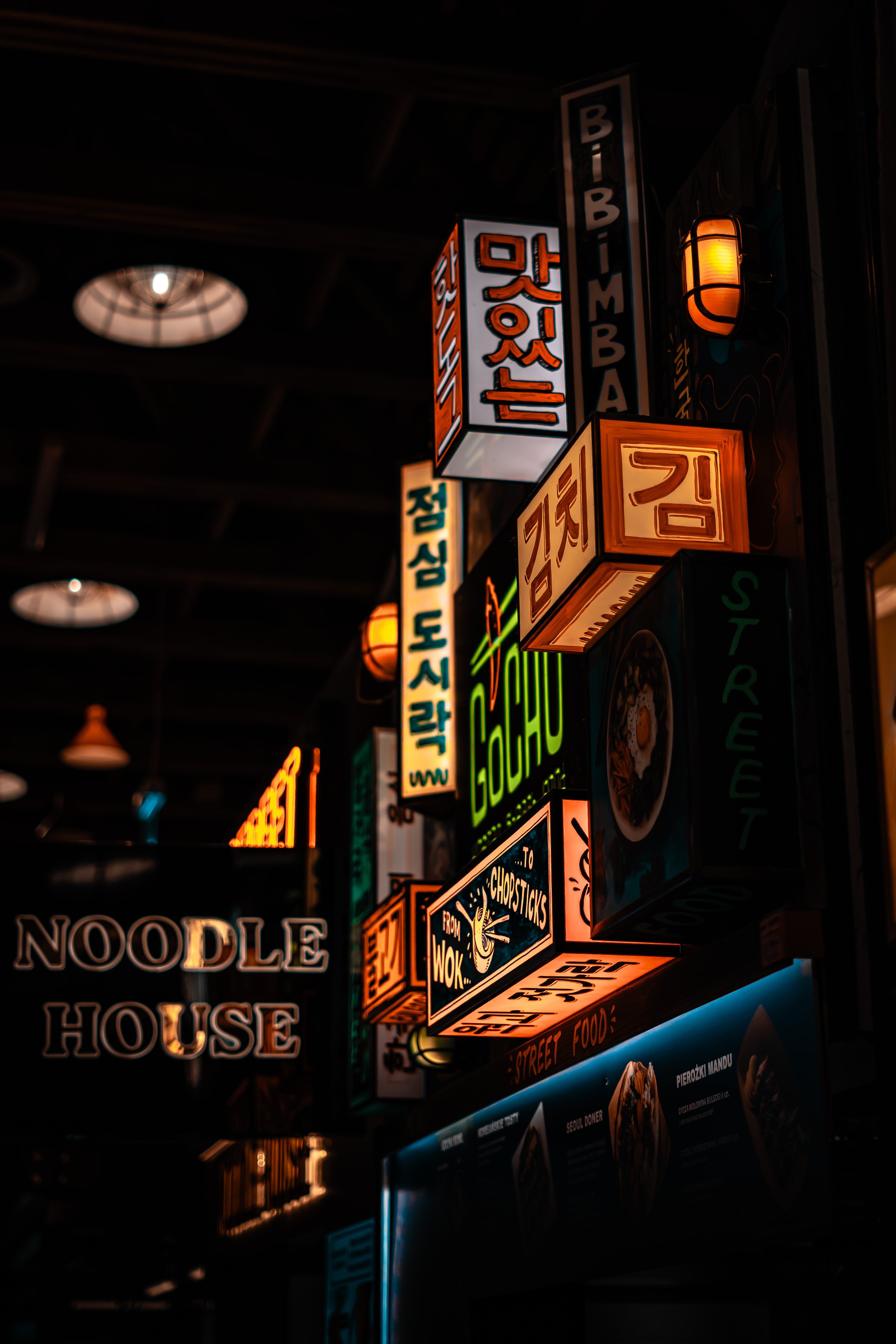 Stacked neon signs above a noodle house counter at night