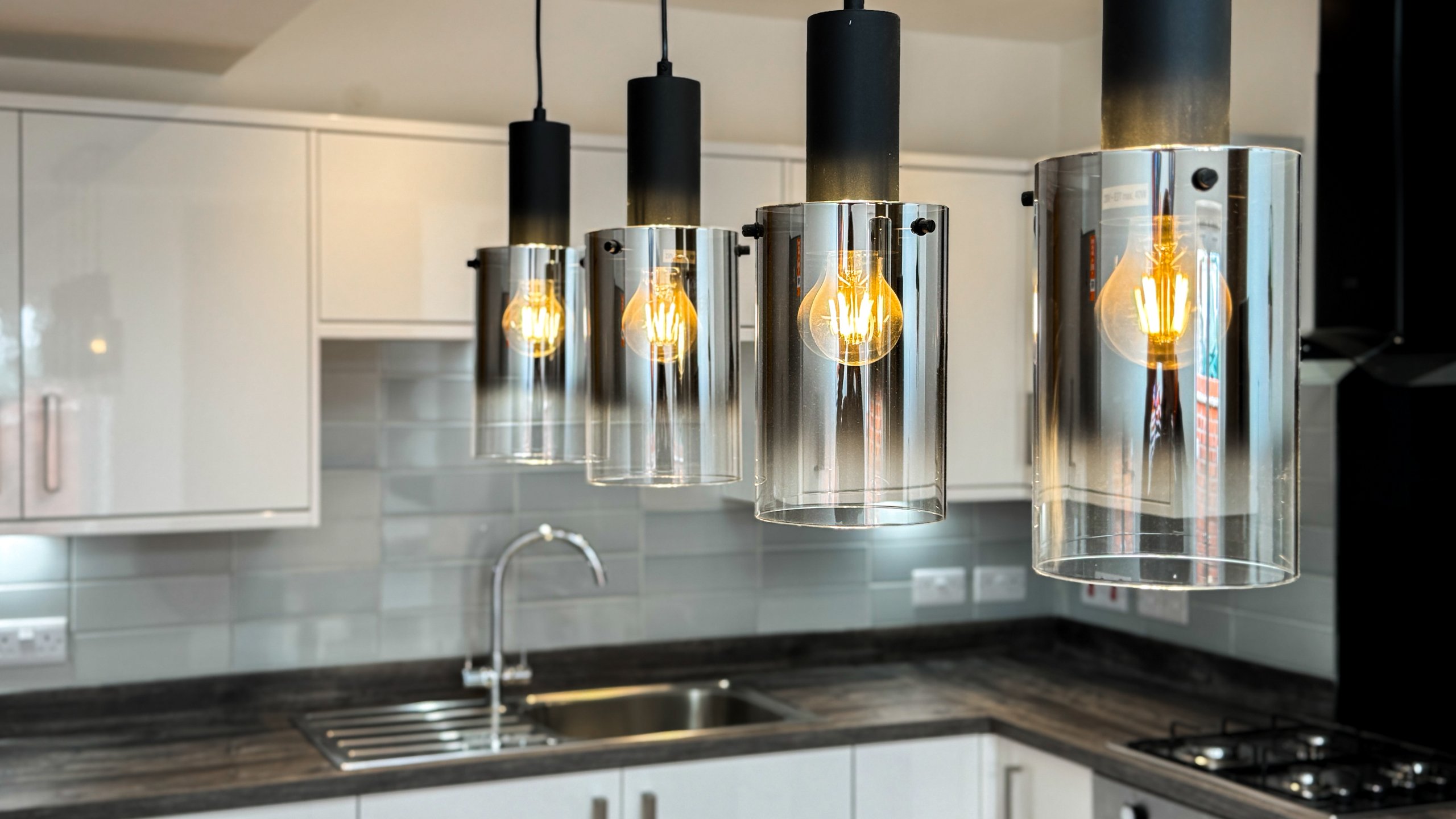 Four smoked glass pendant lights above a kitchen sink and worktop