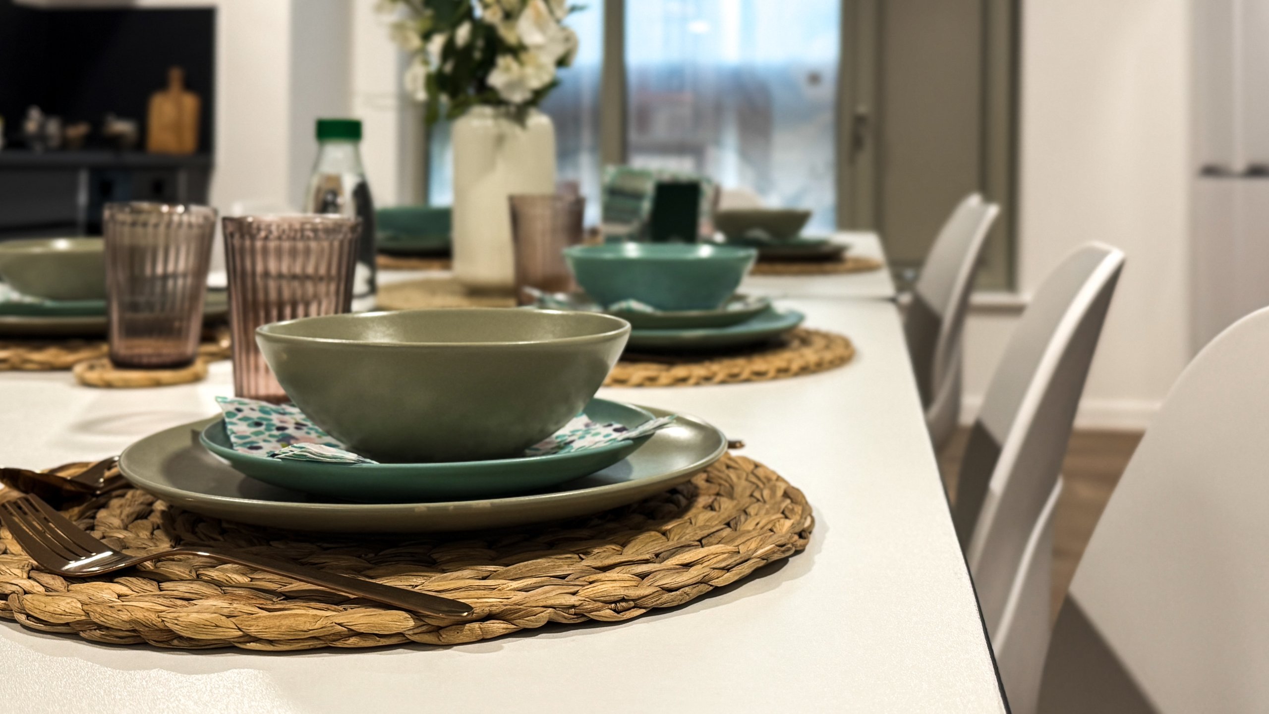 A dining table laid with green crockery, woven mats and glassware