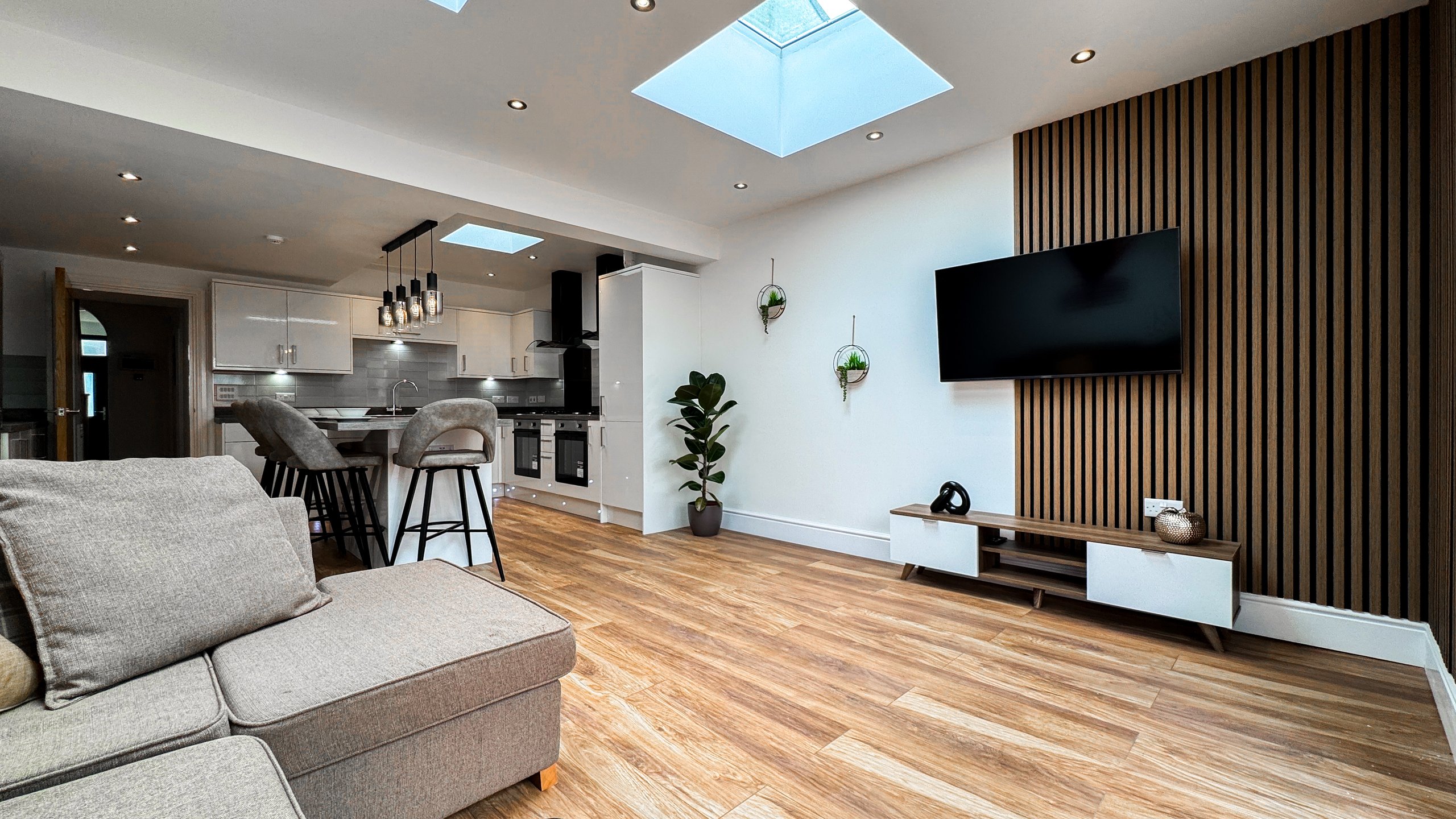 An open plan living room and kitchen with skylights and a slatted timber wall